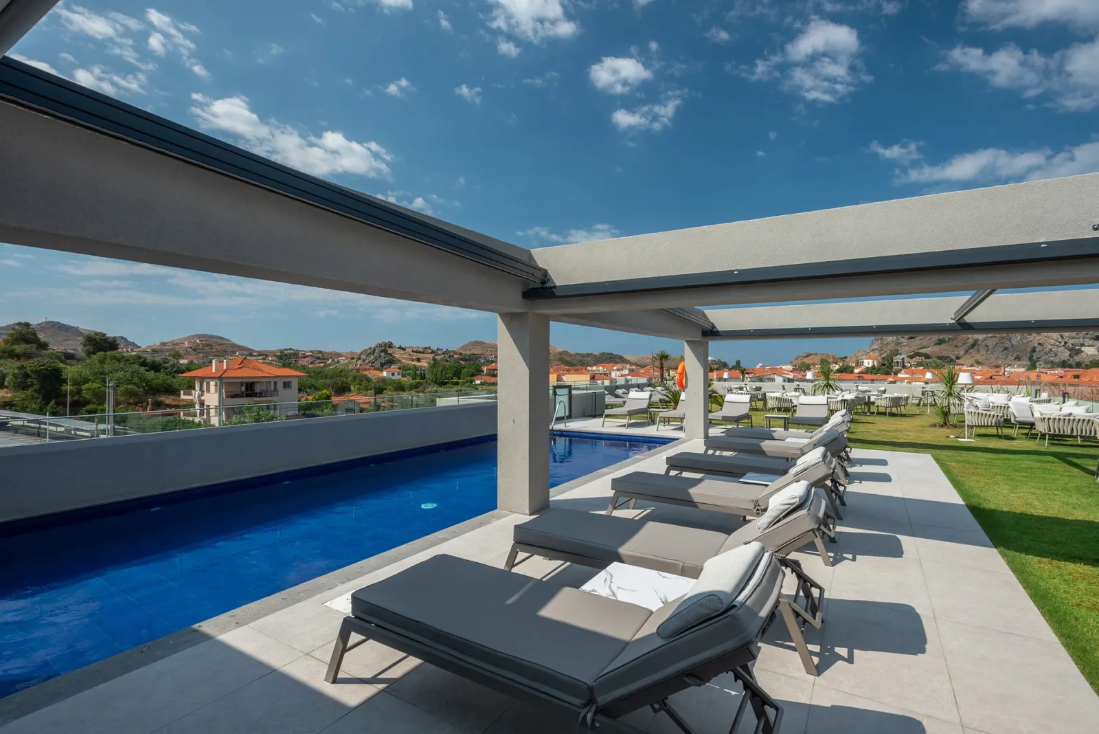 The swimming pool area features comfortable sunbeds and umbrellas, offering a relaxing setting with stunning views of the Castle of Myrina—perfect for moments of leisure under the Greek sun.